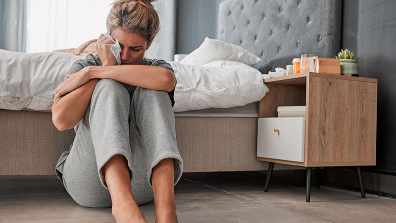Crying sad and depressed woman on bedroom floor