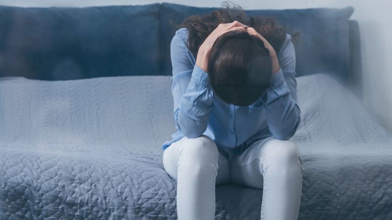 depressed woman sitting on bed and holding head in hands