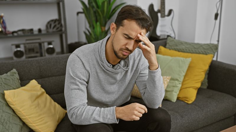 man sitting in the couch feeling dizzy