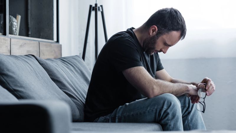 Depressed man holding glasses while sitting