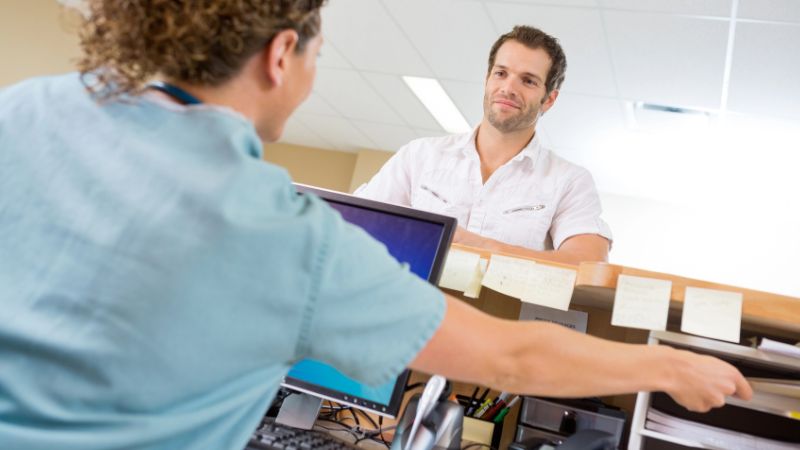 Nurse Assisting Man While Working At Reception Desk