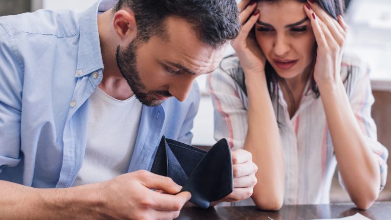 Man looking at empty purse near stressed woman