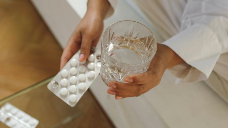 person holding a glass of water and medicine