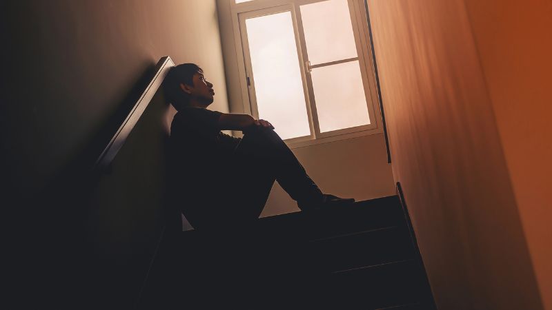 Sad young man sitting at the stairs in the dark