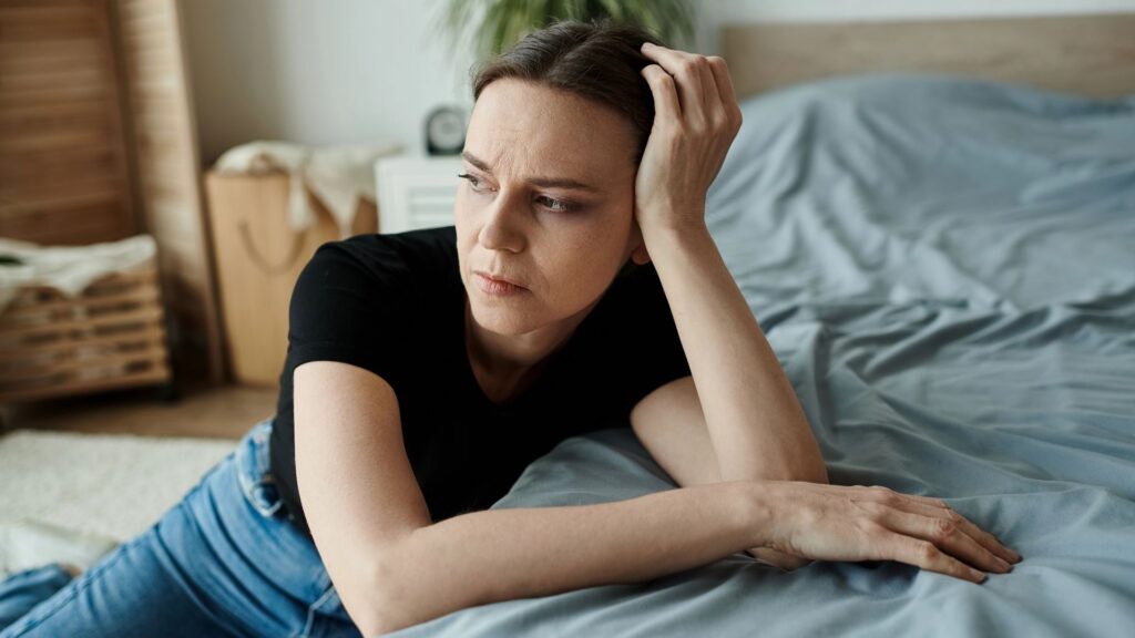 Middle-aged woman lying on bed with head in hands, showing signs of depression.
