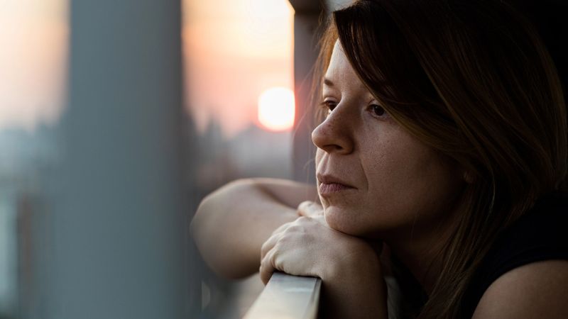 Young sad woman looking outside through balcony