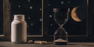 An hourglass and a pill bottle highlighting the long-term side effects of psychiatric drugs.