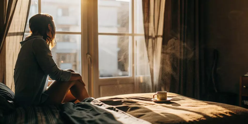 A female experiencing anxiety attack symptoms while sitting alone on her bed.