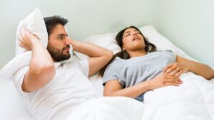 young man covering his ears with his snoring girlfriend while lying bed